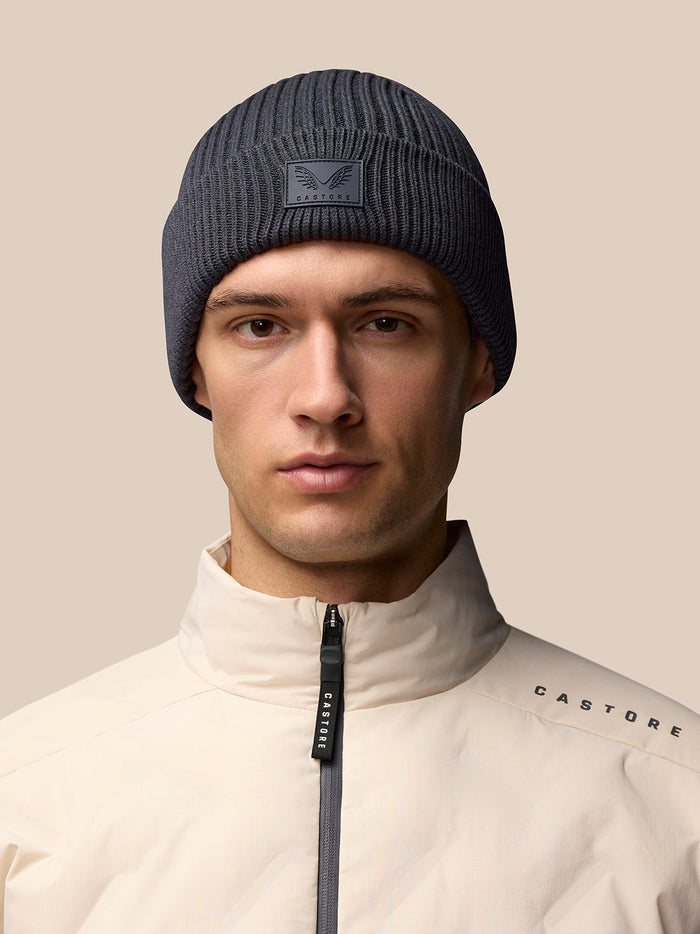 Model wearing a grey Castore beanie with logo on front and beige jacket