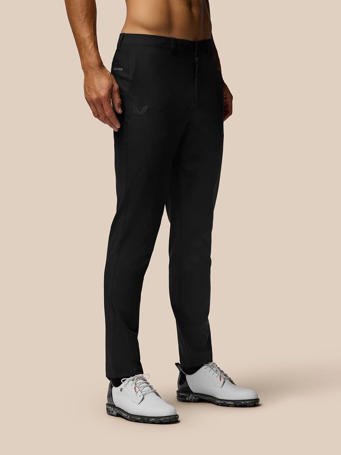 Male model in black golf trousers with belt loops and side pockets; Castore branding on right thigh and right rear waistband, white golf shoes.