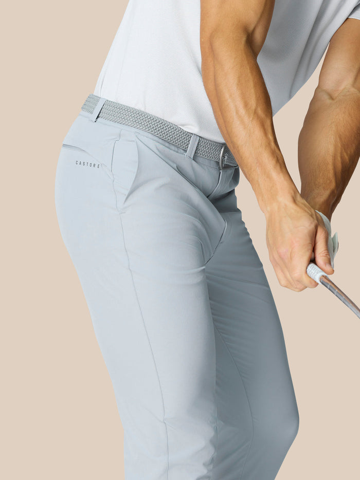 Rear view of light grey golf trousers with braided belt and Castore branding at the back pocket.
