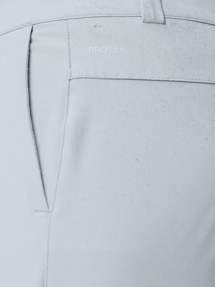 Close-up of light grey golf trouser fabric showing ProTek water resistant technology and pocket stitching.