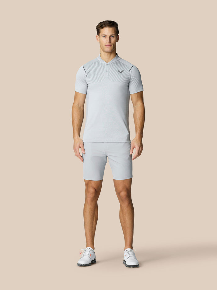 Full-body shot of a male model wearing light grey golf shorts and a matching polo on a beige background.
