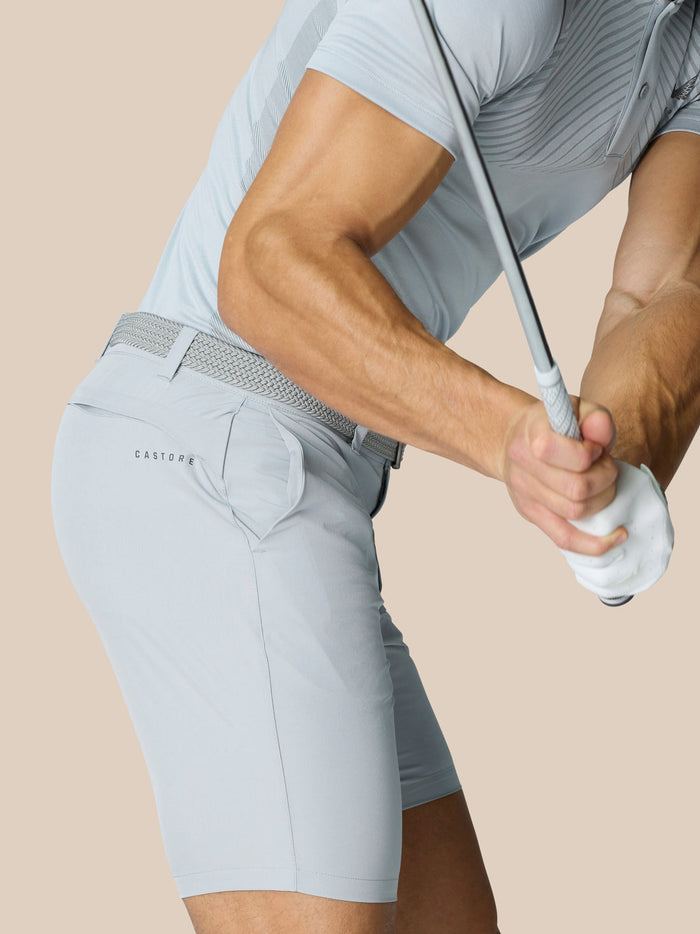 Side view of a golfer wearing light grey shorts with braided belt while swinging a club with Castore branding on the hip