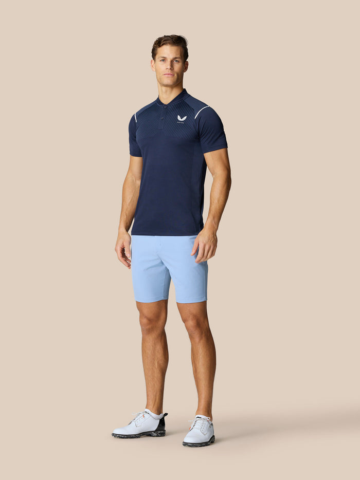 Male model wearing sky blue golf shorts with navy polo on a beige background
