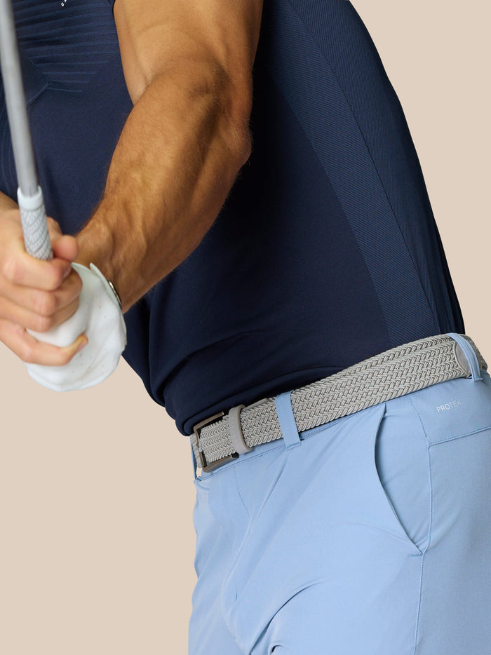 Golfer in navy shirt and light blue golf shorts with braided belt mid swing focusing on the waist area