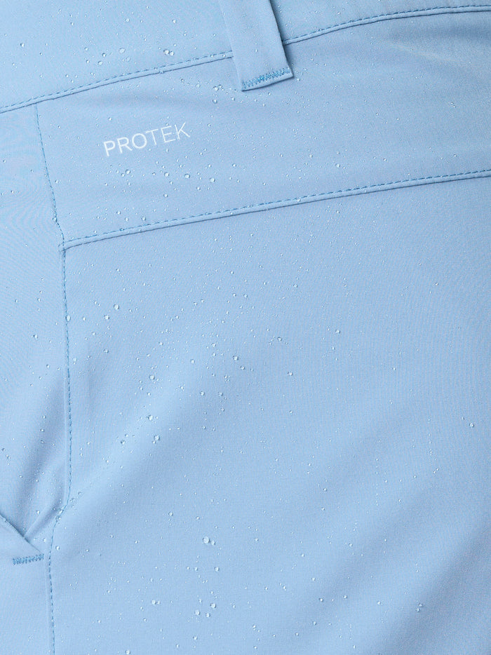 Close-up of sky blue golf shorts fabric with water droplets and ProTek branding near the belt loop