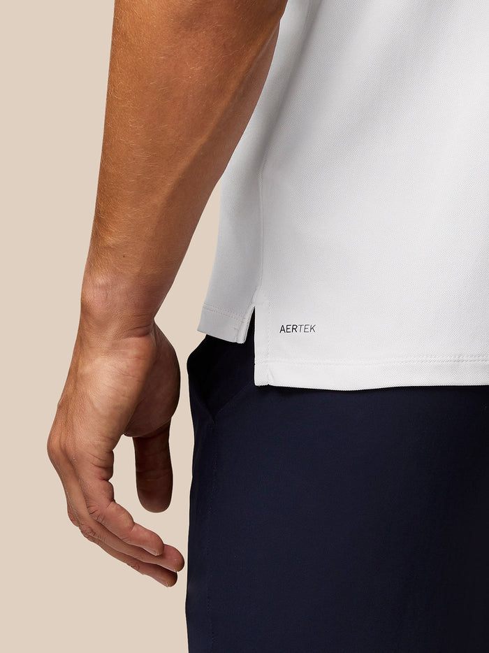 Close up of the polo hem showing AERTEK branding and a side vent on the white Golf Club Essential Polo