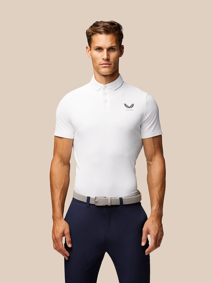 Male model wearing white Golf Club Essential Polo with Castore logo on the chest against a beige backdrop