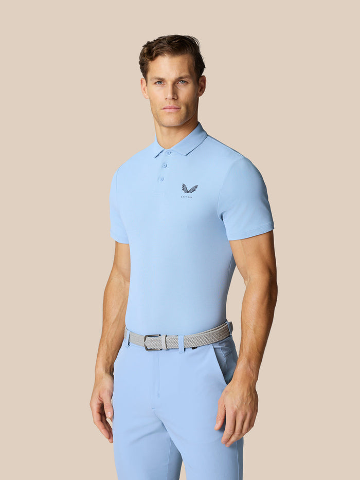 Male model wearing sky blue Golf Club Essential Polo with collar short sleeves and left chest logo.