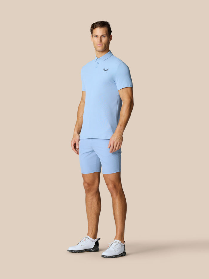 Male model in sky blue Golf Club Essential Polo and matching shorts with white golf shoes.