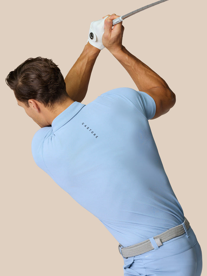 Golfer in sky blue polo mid backswing with a light gray belt and a Castore logo on the back of the shirt