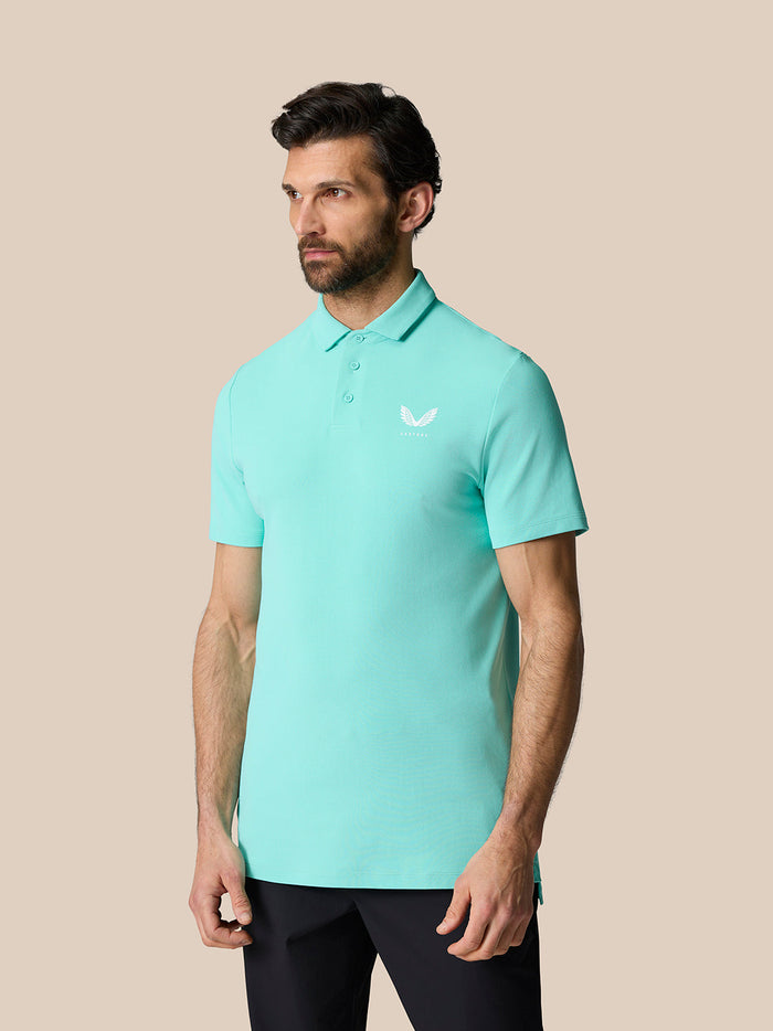 Three quarter view of a man in a light aqua Golf Club Essential Polo with a white Castore logo, paired with dark trousers.