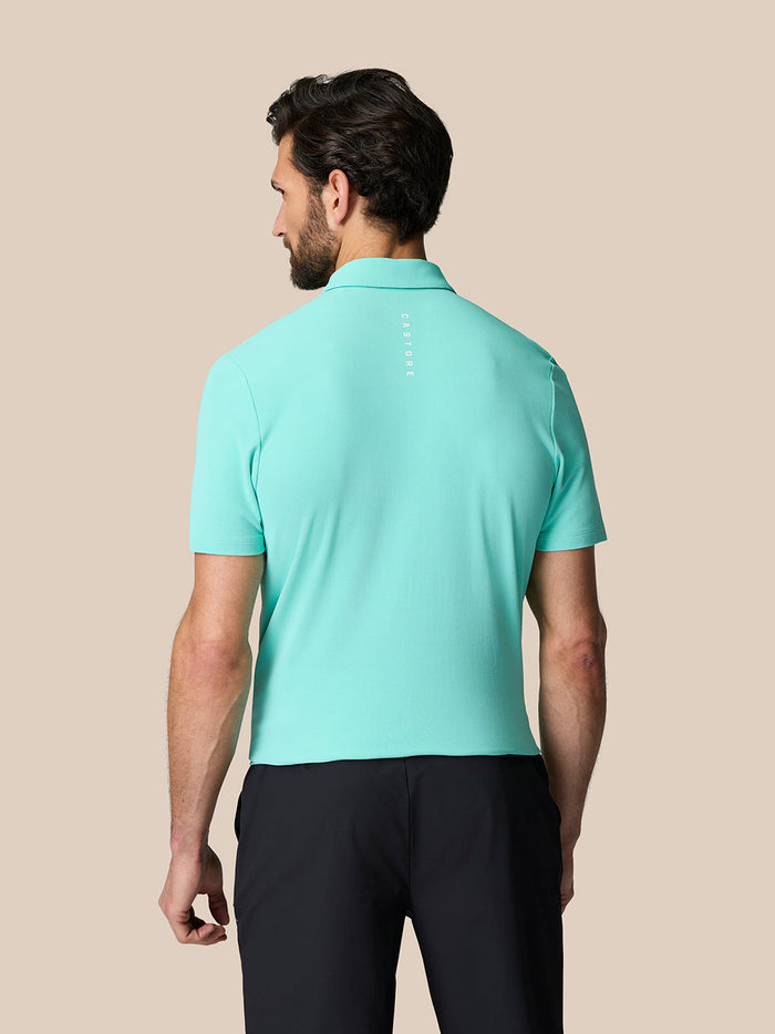 Back view of a man in a light aqua Golf Club Essential Polo with Castore branding running down the back.