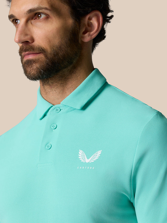 Close up of a man wearing a light aqua Golf Club Essential Polo with a left chest Castore logo.