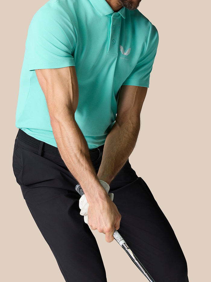 Back and shoulder view of a man in a light aqua Golf Club Essential Polo with Castore logo on the chest and vertical branding.