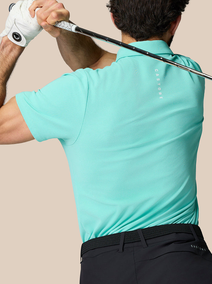 Golfer in a light aqua Golf Club Essential Polo mid swing holding a club with Castore branding on the back.