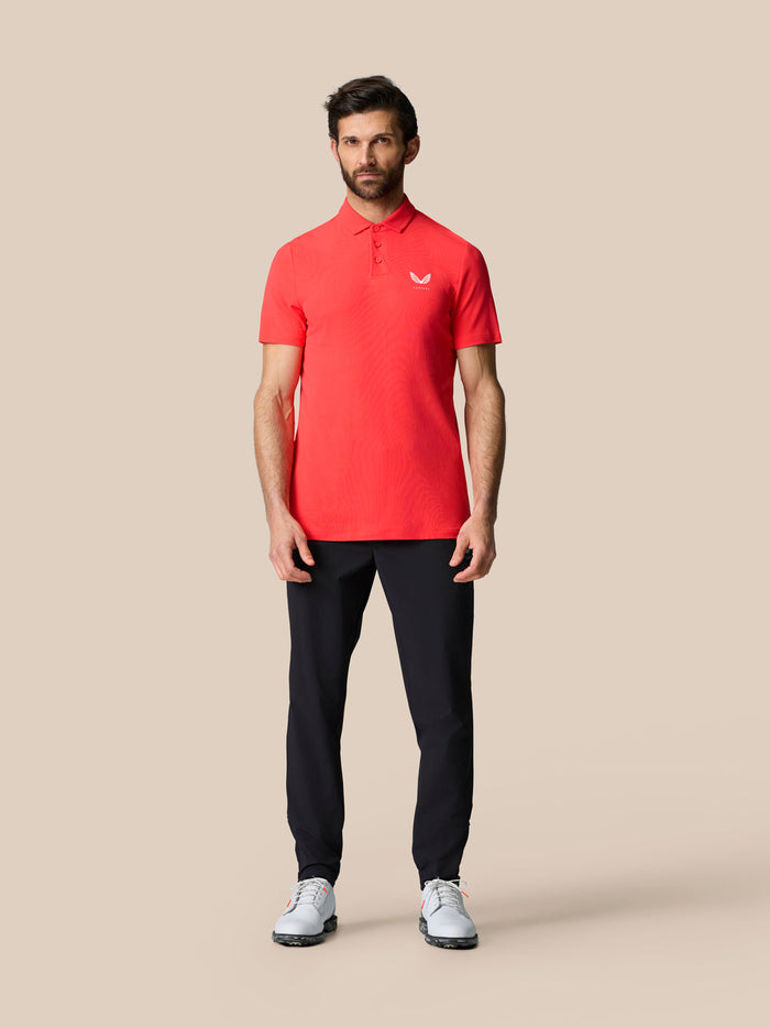 Full-length view of a man in the red Golf Club Essential Polo with navy pants and white golf shoes.