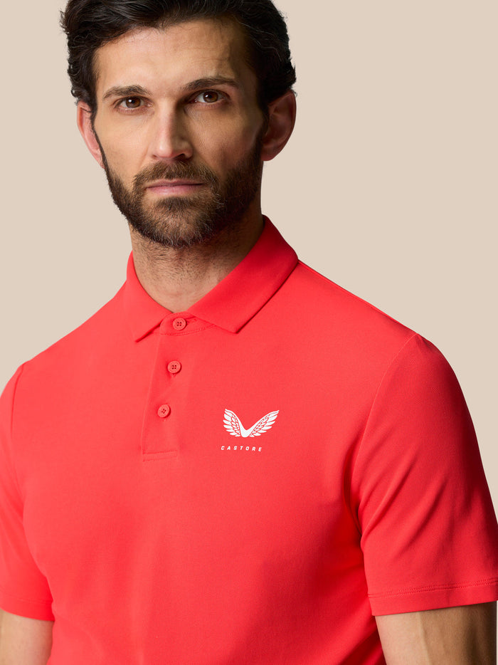 Close-up of coral Golf Club Essential Polo front left chest with white Castore logo.