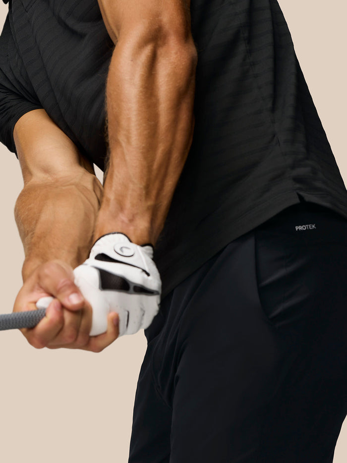 Side view of a man wearing the black Pinnacle polo with vertical Castore logo on the upper back and striped knit