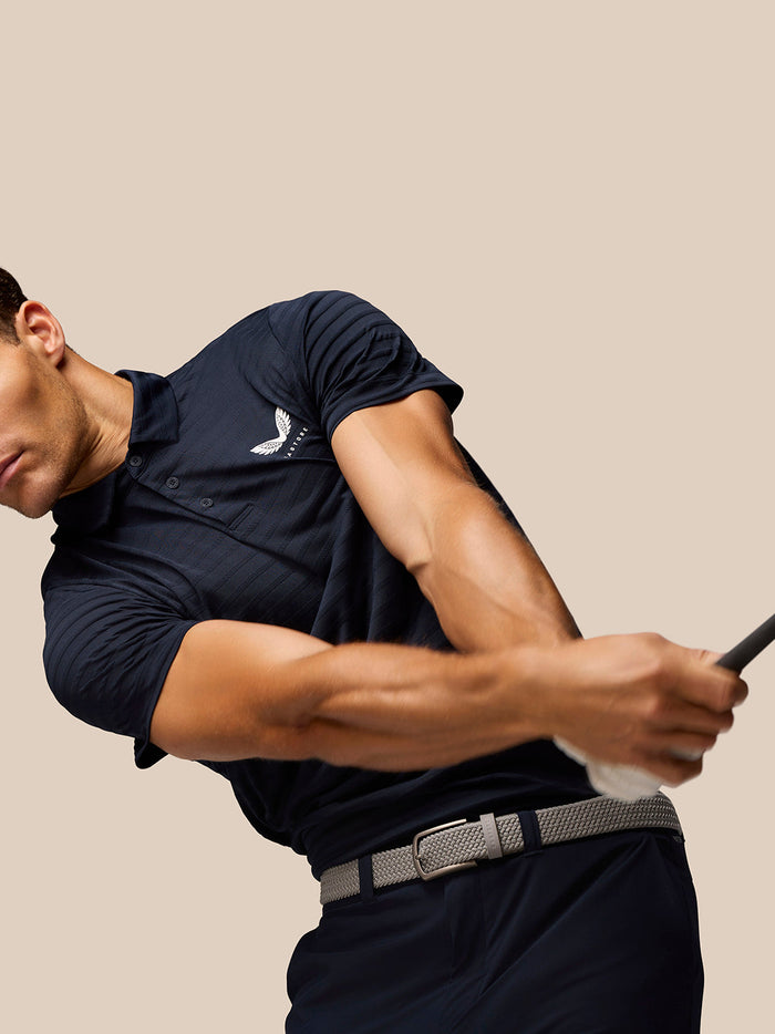 Male model in navy Pinnacle Pique Stripe Polo with stripe fabric and three button collar, Castore logo on chest