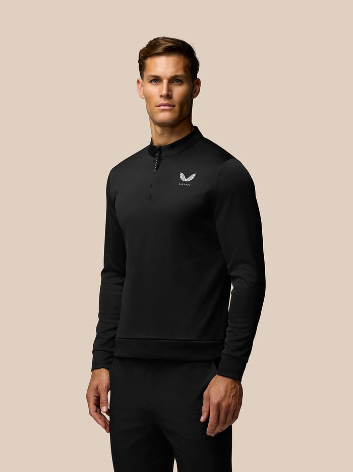 Black quarter zip golf top on a model with white Castore logo on the left chest and vertical Castore branding on the upper back.