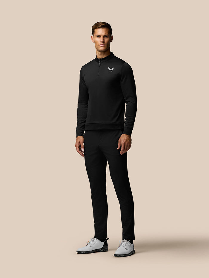 Model wearing black Castore Golf Club Classic 1/4 Zip Top with matching golf pants and white shoes.