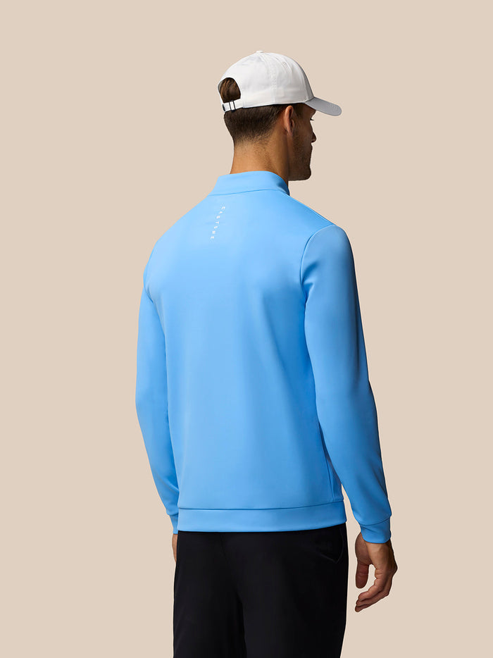 Back view of a male model wearing a cool blue golf club classic quarter zip top with a white cap