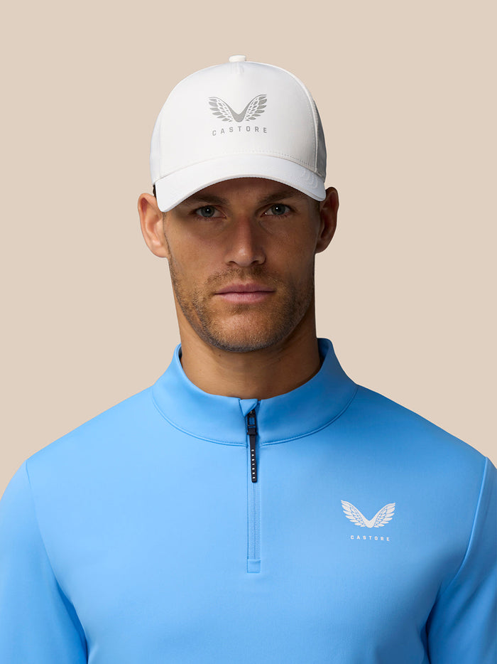 Front view of a man wearing a white cap and sky blue Club Classic quarter-zip top, with Castore logo on the left chest.
