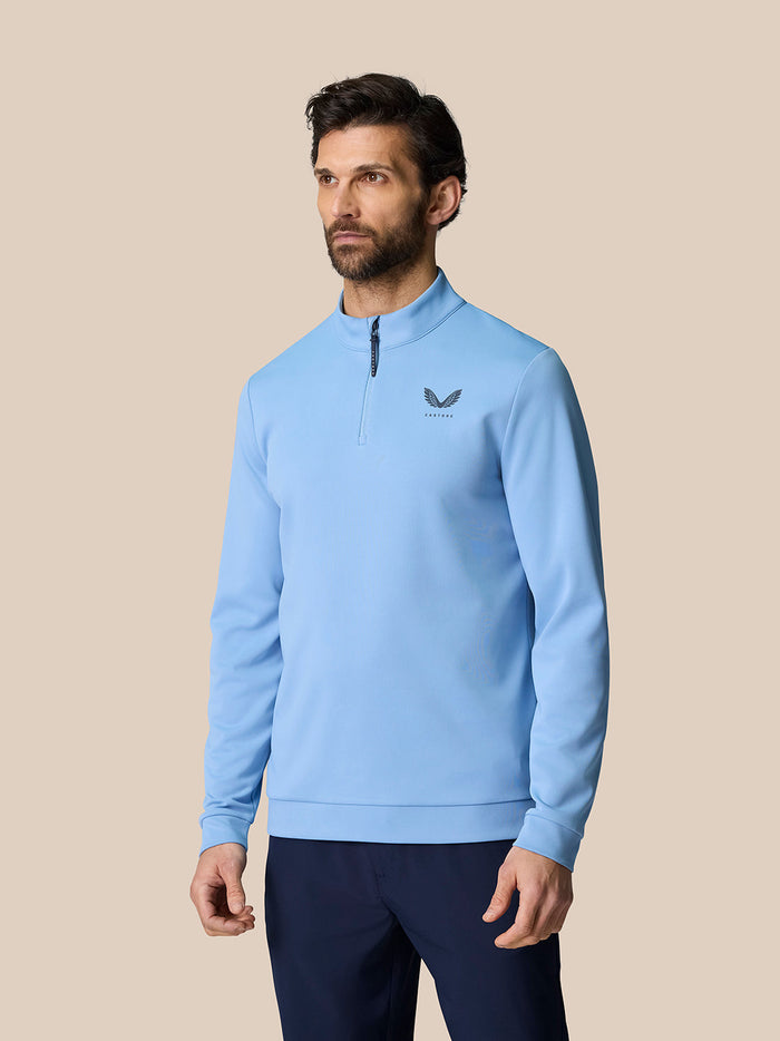 Male model wearing sky blue Golf Club Classic Quarter Zip Top with stand collar and front 1/4 zip Castore logo on the chest
