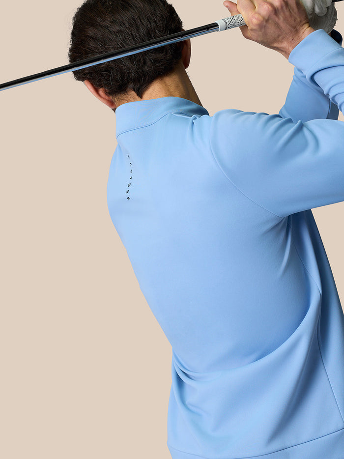 Back view of a golfer wearing a sky blue Castore Golf Club Classic Quarter Zip Top while swinging a club.