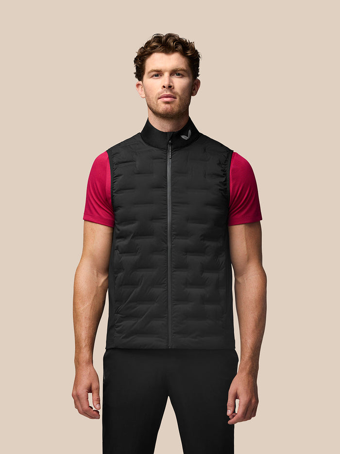 Front view of a man wearing a black Golf Pinnacle Gilet with a stand collar over a pink short sleeve shirt.