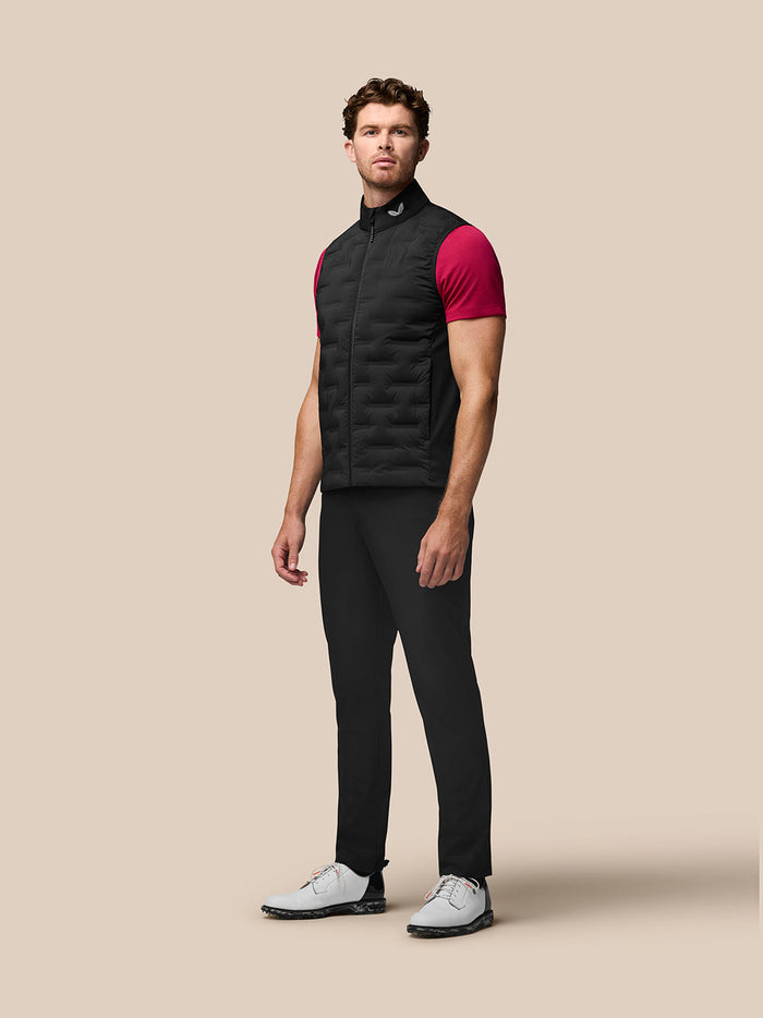 Male model wearing black Golf Pinnacle Gilet over a pink T shirt with stand collar.