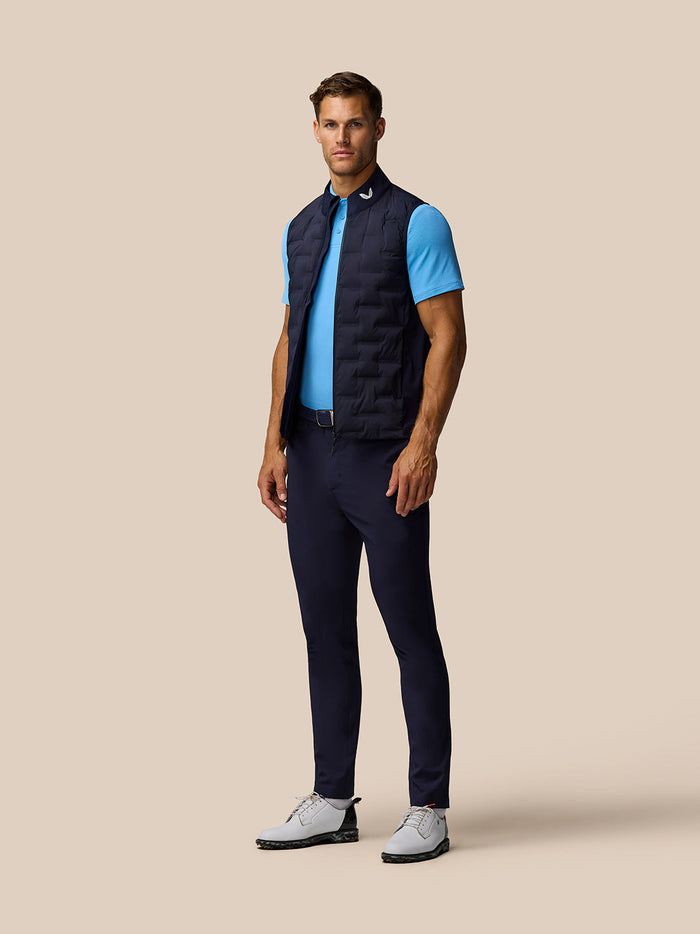 Full body shot of a man in midnight navy Golf Pinnacle Gilet over a blue polo, navy pants and white shoes