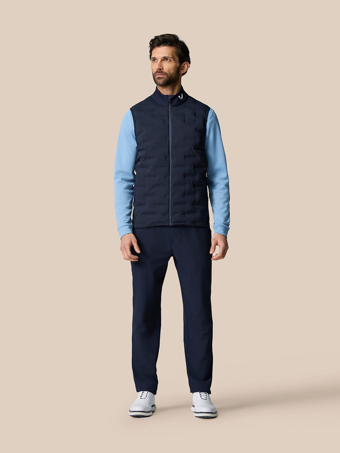 Male model wearing Golf Pinnacle Gilet in midnight navy with light blue sleeves on beige backdrop