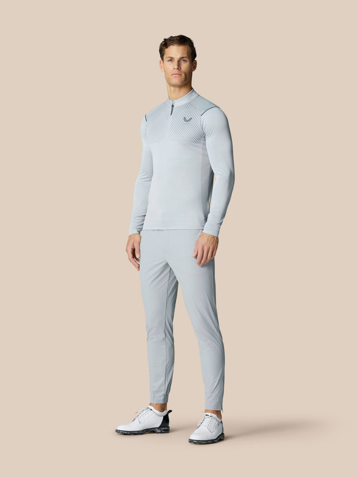 Male model wearing light grey golf outfit featuring Pinnacle 32 trousers and matching top against a beige background.