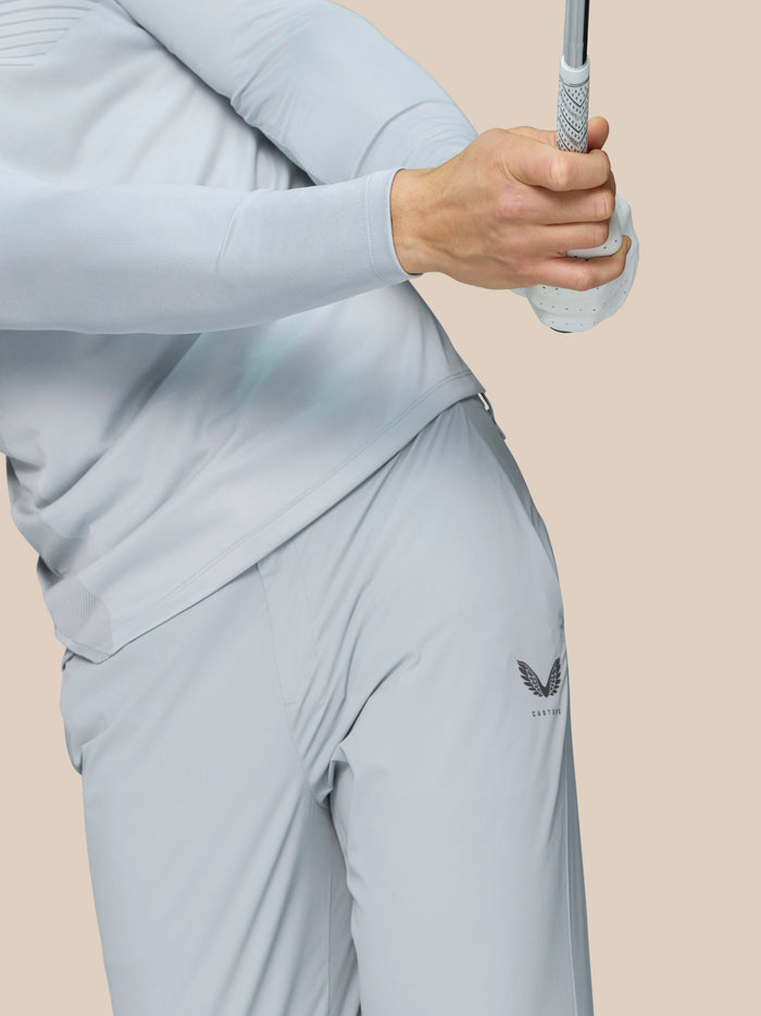Side view of golfer in pale grey athletic top with diagonal pattern and Castore logo on the hip while holding a club.