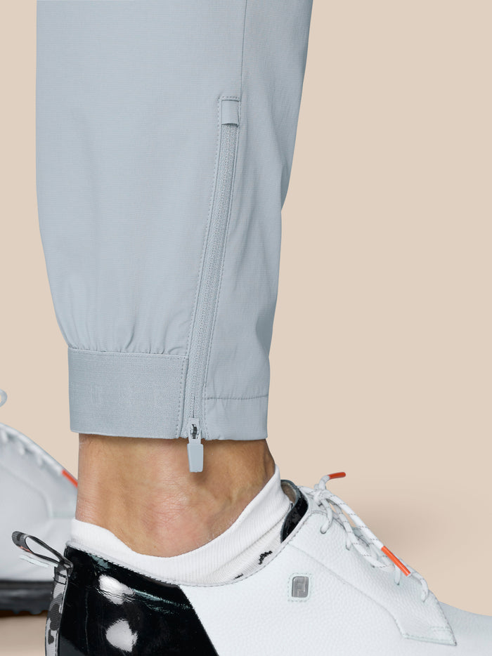 Close-up of light grey golf trousers showing a zip at the lower leg hem