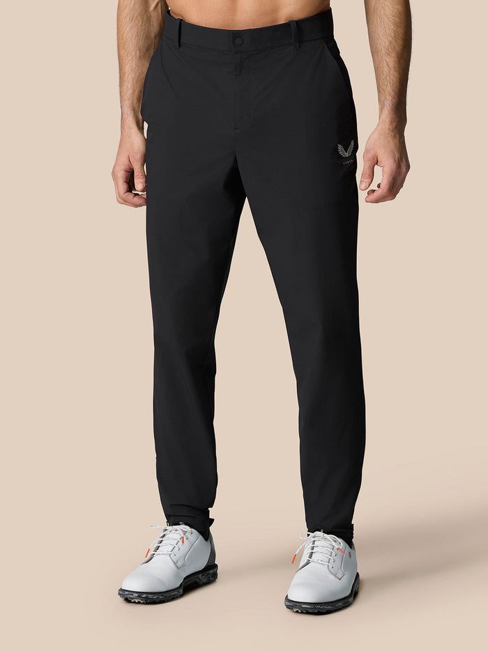 Male model in black Golf Pinnacle 32 trousers with logo on right thigh and white sneakers