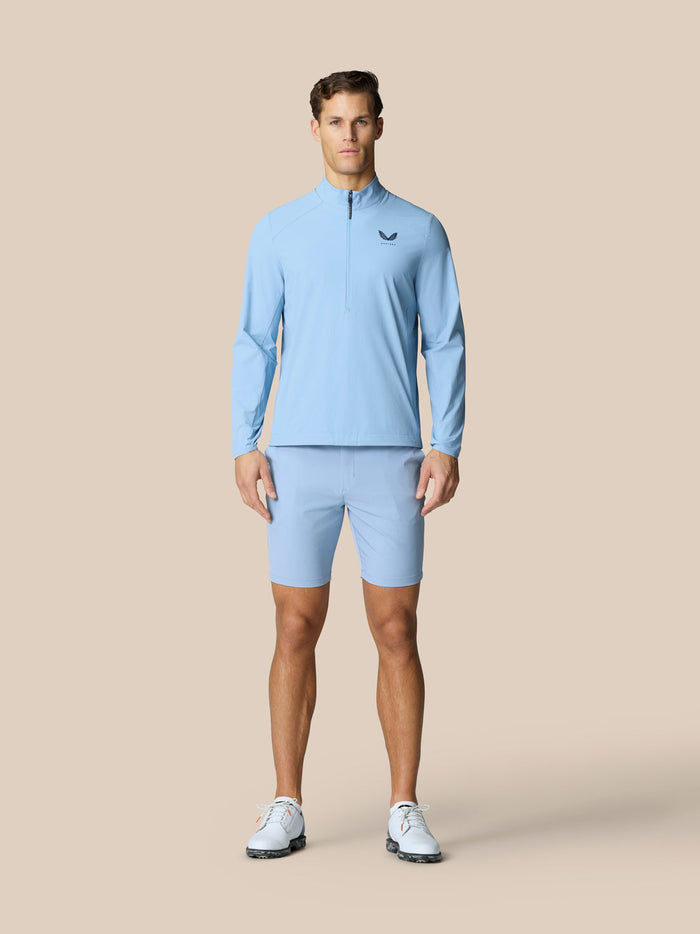 Full body front view of a man wearing the sky blue Golf Flex Woven Half Zip jacket with matching shorts and white sneakers