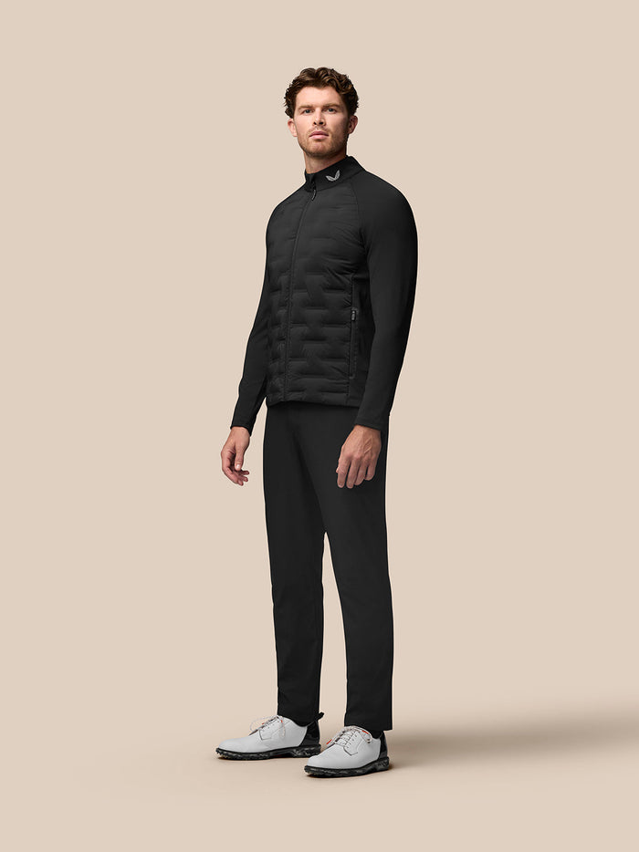 Full body view of a male model in black Golf Pinnacle Jacket with matching pants and white sneakers against a beige backdrop.