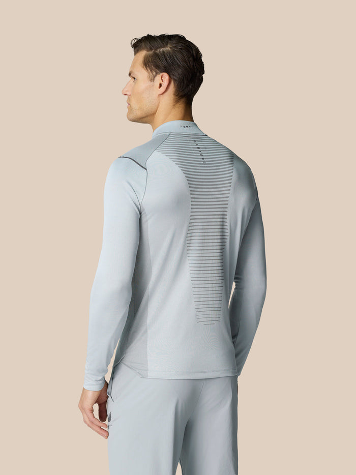 Back view of a man in a light grey Pinnacle LVS 1/4 zip top featuring vertical vent stripes along the back.