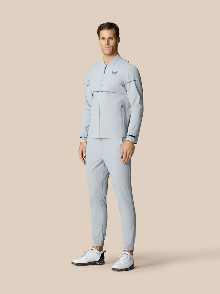 Male model wearing Golf Pinnacle LVS Woven Jacket in mid grey with matching pants and white golf shoes
