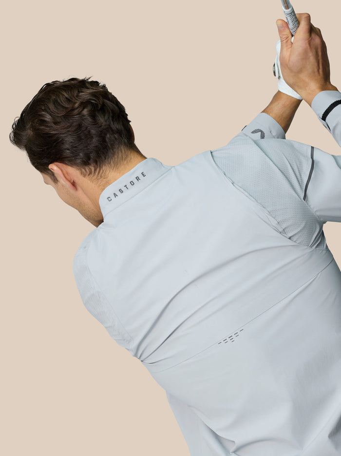 Rear view of a man in the Golf Pinnacle LVS Woven Jacket showing Castore branding on the neck while swinging a club