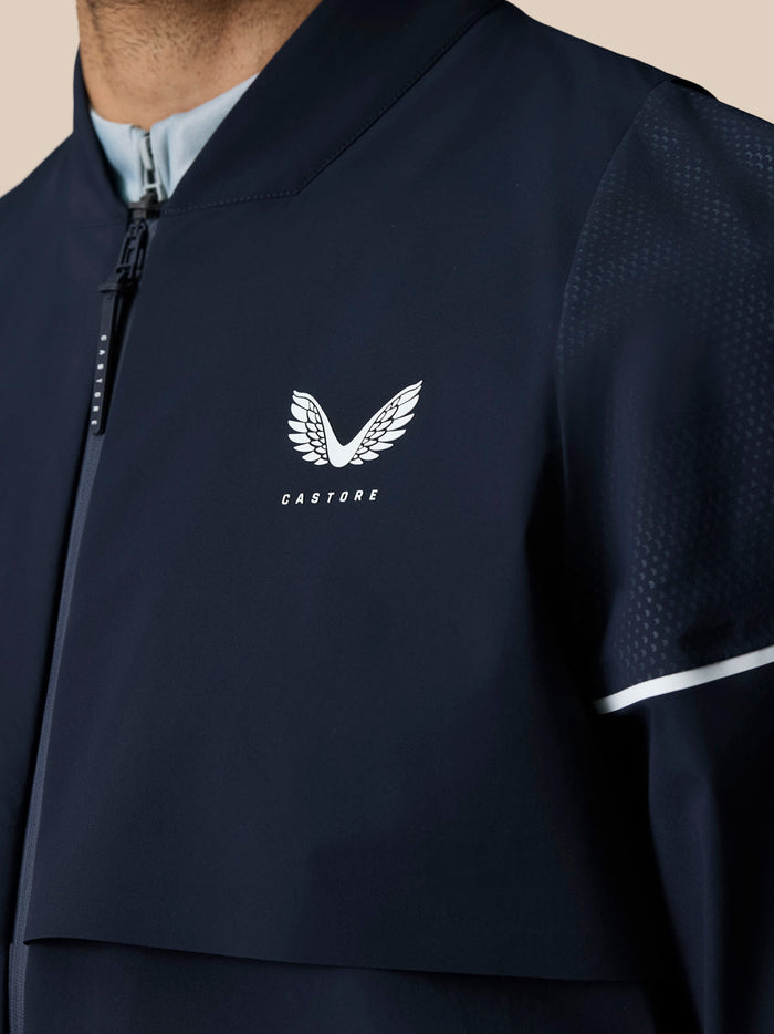 Close-up of navy Pinnacle LVS jacket chest showing the white Castore wing logo and front zipper