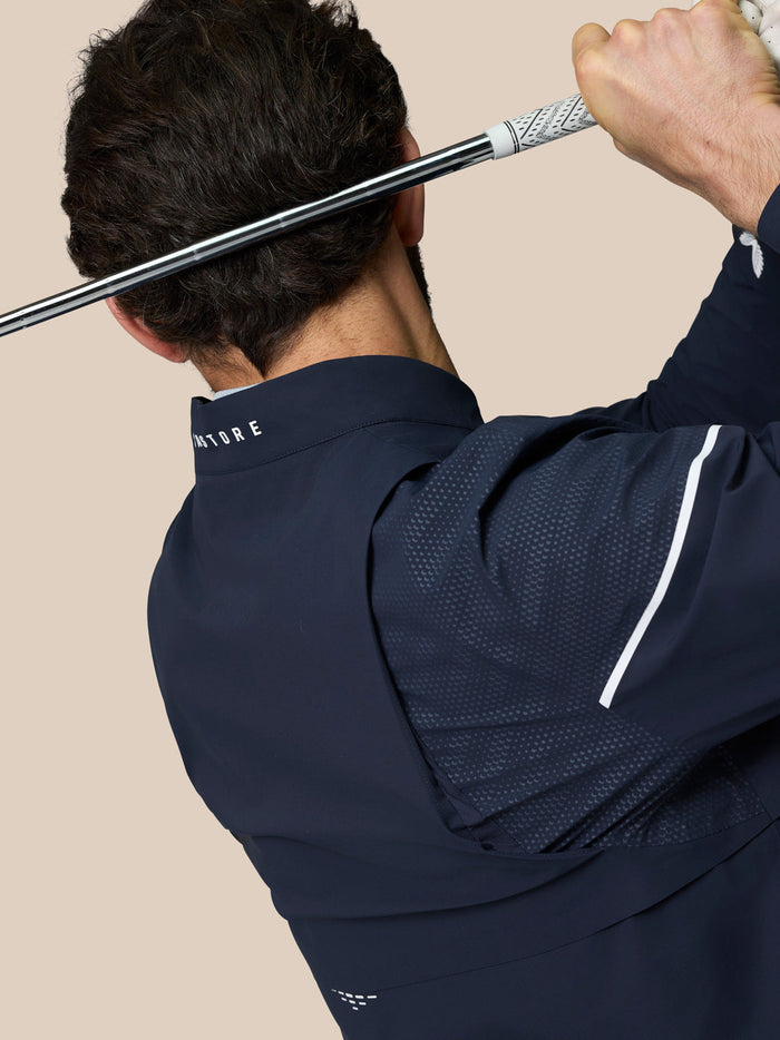 Golfer wearing Golf Pinnacle LVS Woven Jacket in midnight navy back view during a swing