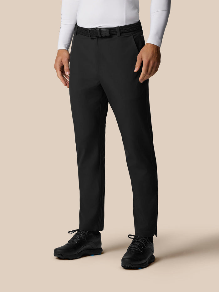 Front view of a male model wearing black Golf Pinnacle Winter Trousers with a white top and black belt.