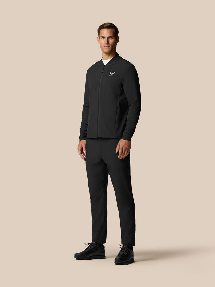 Full-body shot of a male model in a black winter golf outfit featuring a zip jacket and matching trousers.