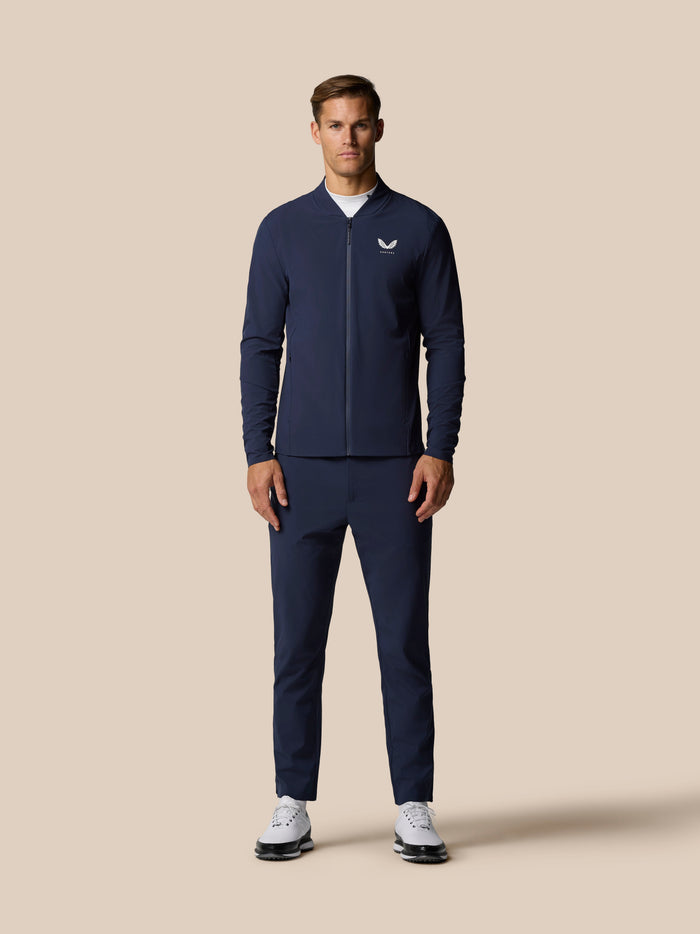Male model wearing navy zip front bomber jacket with crest logo against beige background
