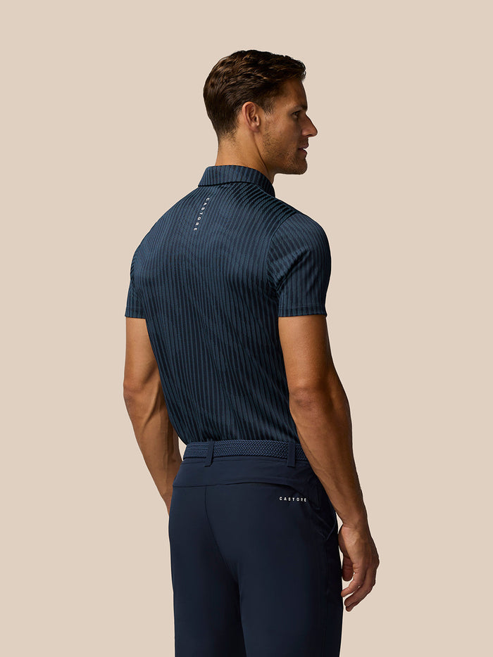 Back view of a man wearing a navy all over striped Golf Pinnacle Glow Polo.
