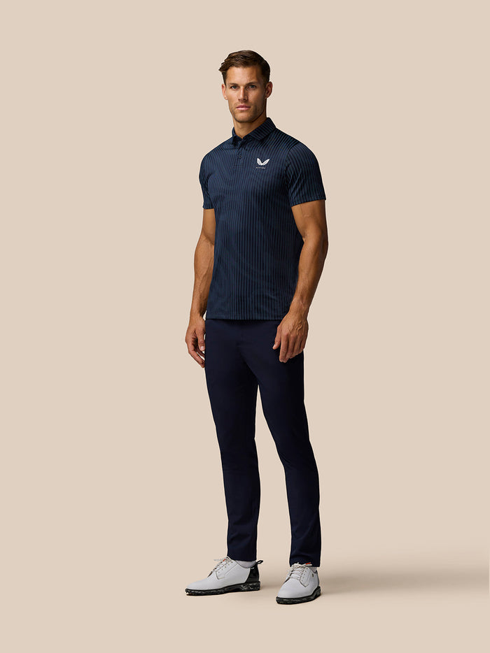 Full body shot of a man in a navy striped Golf Pinnacle Glow Polo with Castore logo on the chest and navy pants.