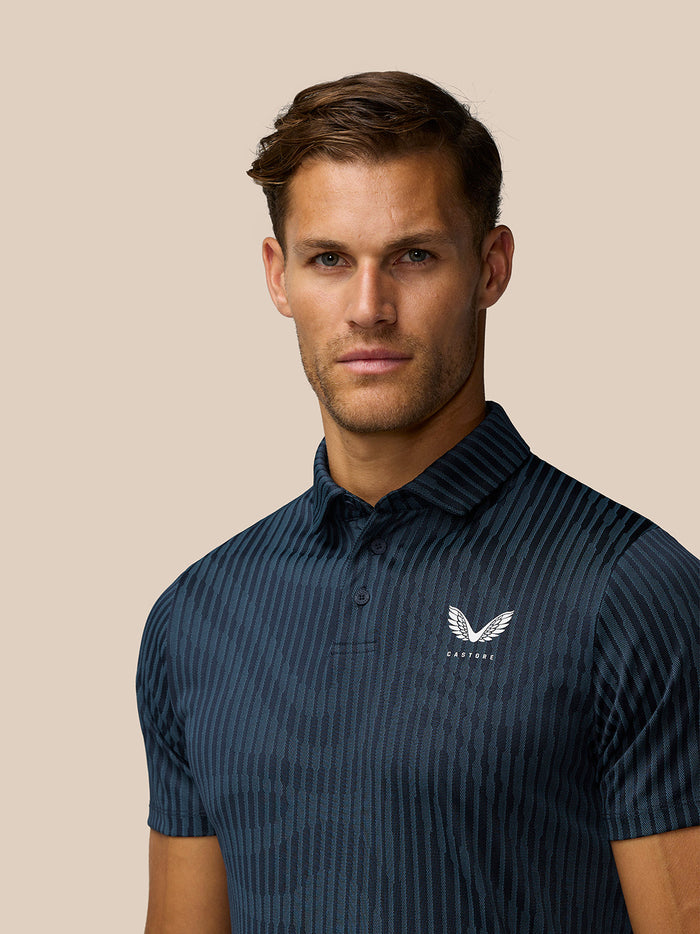 Close-up of model in midnight navy Golf Pinnacle Glow Polo showing the striped knit and Castore logo on the left chest.